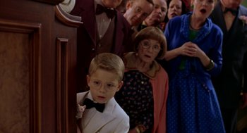 Movie still from “Stuart Little” (1999), directed by Rob Minkoff – A group of people standing in a room with a young boy in a suit; Medium shot, High angle