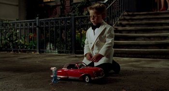 Movie still from “Stuart Little” (1999), directed by Rob Minkoff – A young boy in a white suit is playing with a red toy car; Wide shot, High angle