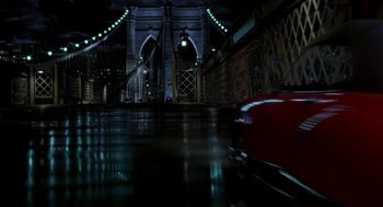Movie still from “Stuart Little” (1999), directed by Rob Minkoff – A red car driving down a street next to a bridge at night; Extreme Wide shot, High angle
