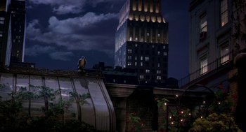 Movie still from “Stuart Little 2” (2002), directed by Rob Minkoff – A bird sitting on top of a roof near a building at night; Extreme Wide shot, Low angle