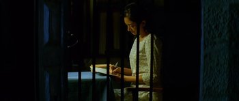A woman writing in a notebook in a jail cell