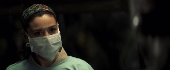 Movie still from “Tears of the Sun” (2003), directed by Antoine Fuqua – A person wearing a surgical mask and a green shirt; Close Up shot, Over the shoulder angle