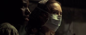 Movie still from “Tears of the Sun” (2003), directed by Antoine Fuqua – A woman wearing a face mask while standing next to a man; Close Up shot, Low angle