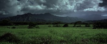Movie still from “Tears of the Sun” (2003), directed by Antoine Fuqua – A grassy field with mountains in the background under a cloudy sky; Extreme Wide shot, High angle