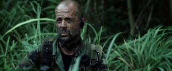 Movie still from “Tears of the Sun” (2003), directed by Antoine Fuqua – A man with a beard is wearing a headset in the woods; Close Up shot, Over the shoulder angle