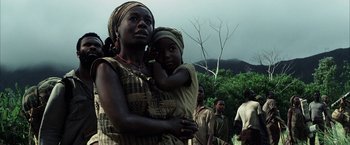 Movie still from “Tears of the Sun” (2003), directed by Antoine Fuqua – A woman holding a child in her arms while standing in front of a group of people; Close Up shot, Low angle