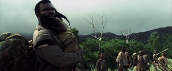 Movie still from “Tears of the Sun” (2003), directed by Antoine Fuqua – A group of people standing in the grass; Medium shot, Low angle