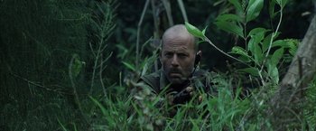 Movie still from “Tears of the Sun” (2003), directed by Antoine Fuqua – A bald man with a beard is sitting in the grass; Close Up shot, Low angle