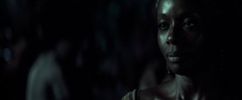 Movie still from “Tears of the Sun” (2003), directed by Antoine Fuqua – A woman is looking at the camera with a dark background; Close Up shot, Over the shoulder angle