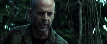 Movie still from “Tears of the Sun” (2003), directed by Antoine Fuqua – A man with a beard and a black shirt is in the woods; Close Up shot, Low angle