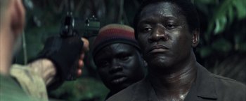 Movie still from “Tears of the Sun” (2003), directed by Antoine Fuqua – A man holding a gun in front of another man; Close Up shot, Low angle