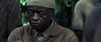 Movie still from “Tears of the Sun” (2003), directed by Antoine Fuqua – An older man wearing a cap and a brown jacket; Close Up shot, High angle