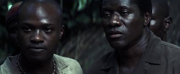 Movie still from “Tears of the Sun” (2003), directed by Antoine Fuqua – Two men standing next to each other near a forest; Close Up shot, Over the shoulder angle