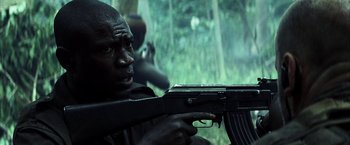 Movie still from “Tears of the Sun” (2003), directed by Antoine Fuqua – A man holding an ak - 4 7 rifle in the woods; Close Up shot, Low angle