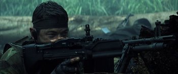 Movie still from “Tears of the Sun” (2003), directed by Antoine Fuqua – A man with a rifle in a field; Close Up shot, Over the shoulder angle