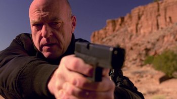 Movie still from “Breaking Bad” (2008), created by Vince Gilligan – A man holding a gun while standing in front of a mountain; Close Up shot, Low angle