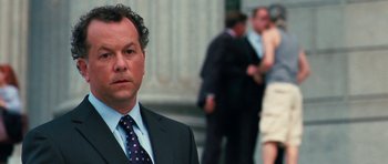 Movie still from “The Bounty Hunter” (2010), directed by Andy Tennant – A man in a suit and tie standing in front of a group of people; Close Up shot, Over the shoulder angle