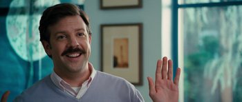 Movie still from “The Bounty Hunter” (2010), directed by Andy Tennant – A man with a mustache waving at the camera; Close Up shot, Over the shoulder angle