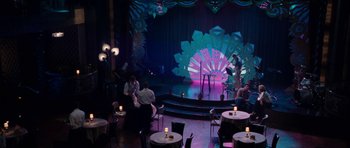 Movie still from “The Bounty Hunter” (2010), directed by Andy Tennant – People sitting at tables in front of a stage with lights; Extreme Wide shot, High angle