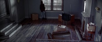 Movie still from “The Cable Guy” (1996), directed by Ben Stiller – A person standing in a living room looking out a window; Wide shot, High angle