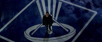 Movie still from “The Cable Guy” (1996), directed by Ben Stiller – A man standing in a room with a clock on the ground; Extreme Wide shot, Overhead angle