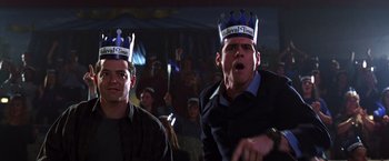 Movie still from “The Cable Guy” (1996), directed by Ben Stiller – Two men wearing paper crowns in front of an audience; Medium shot, Low angle