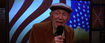 Movie still from “The Cable Guy” (1996), directed by Ben Stiller – An older man is holding a microphone in his hand; Close Up shot, High angle