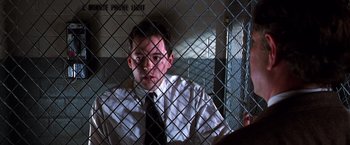 Movie still from “The Cable Guy” (1996), directed by Ben Stiller – A man wearing a white shirt and a black tie behind a metal fence; Close Up shot, Low angle