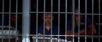 Movie still from “The Cable Guy” (1996), directed by Ben Stiller – A man sitting behind bars in a jail cell; Medium shot, Low angle