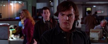 Movie still from “The Cable Guy” (1996), directed by Ben Stiller – A man in a black jacket standing in front of another man; Close Up shot, Over the shoulder angle