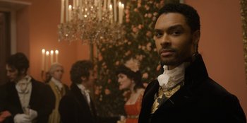 Movie still from “Bridgerton” (2020), created by Chris Van Dusen – A man standing in front of other people in front of a chandelier; Close Up shot, Over the shoulder angle