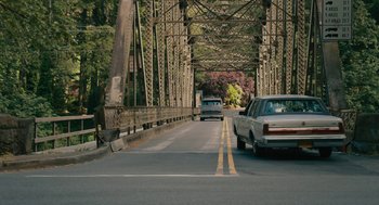 Movie still from “Air” (2023), directed by Ben Affleck – Cars driving down a road under an old bridge; Extreme Wide shot, High angle