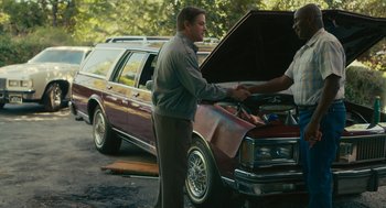 Movie still from “Air” (2023), directed by Ben Affleck – A man standing in front of an open car hood; Medium shot, Over the shoulder angle