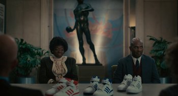 Movie still from “Air” (2023), directed by Ben Affleck – A couple of people sitting at a table with some shoes; Medium shot, Low angle