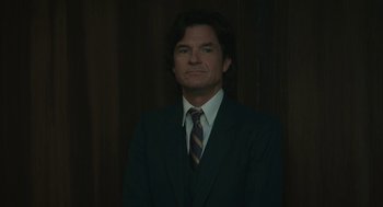 Movie still from “Air” (2023), directed by Ben Affleck – A man wearing a suit and tie standing in front of a wooden wall; Close Up shot, Low angle