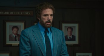Movie still from “Air” (2023), directed by Ben Affleck – Ben affleck in a suit and tie in front of a picture of himself; Medium shot, Over the shoulder angle