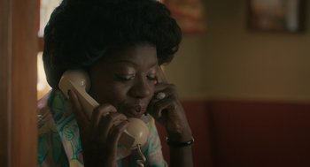 Movie still from “Air” (2023), directed by Ben Affleck – A woman talking on a phone while sitting on a couch; Close Up shot, High angle