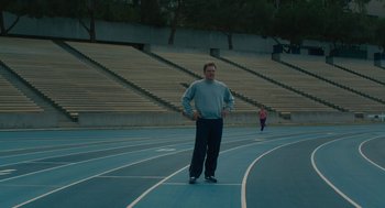 Movie still from “Air” (2023), directed by Ben Affleck – A man standing on a track in front of bleachers; Wide shot, High angle