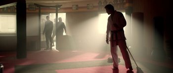 Movie still from “The Debt Collector” (2018), directed by Jesse V. Johnson – A man in a karate uniform stands on a mat in a dojo; Wide shot, Low angle