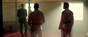 Movie still from “The Debt Collector” (2018), directed by Jesse V. Johnson – A group of people standing in a room with smoke coming out of the windows; Medium shot, Over the shoulder angle