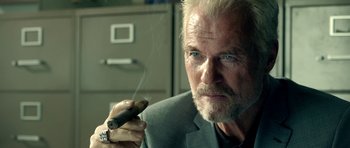 Movie still from “The Debt Collector” (2018), directed by Jesse V. Johnson – An older man smoking a cigar in a room; Close Up shot, Low angle