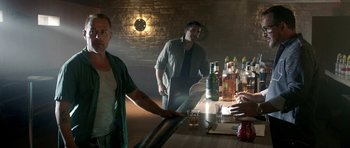 Movie still from “The Debt Collector” (2018), directed by Jesse V. Johnson – A man standing in front of a table with a bottle of alcohol; Medium shot, Over the shoulder angle