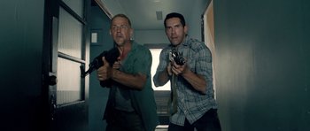Movie still from “The Debt Collector” (2018), directed by Jesse V. Johnson – A couple of men standing next to each other holding guns; Medium shot, Low angle