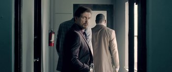 Movie still from “The Debt Collector” (2018), directed by Jesse V. Johnson – A man in a suit standing in front of two other men; Medium shot, Over the shoulder angle