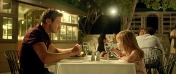 Movie still from “The Debt Collector” (2018), directed by Jesse V. Johnson – A man and a little girl sitting at a dinner table; Medium shot, Over the shoulder angle