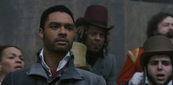 Movie still from “Bridgerton” (2020), created by Chris Van Dusen – A man with a beard and a hat is standing next to another man with dreadlocks; Close Up shot, Over the shoulder angle