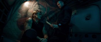 Movie still from “The Expendables” (2010), directed by Sylvester Stallone – Two men sitting in a dark room holding a baseball bat; Medium shot, Low angle