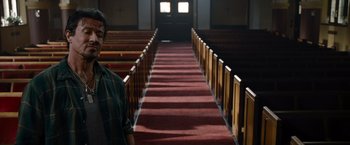Movie still from “The Expendables” (2010), directed by Sylvester Stallone – A person standing in front of a red carpet in a church; Medium shot, Low angle