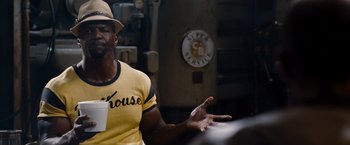 Movie still from “The Expendables” (2010), directed by Sylvester Stallone – A man wearing a yellow shirt and a hat; Medium shot, Over the shoulder angle