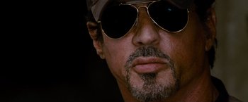 Movie still from “The Expendables” (2010), directed by Sylvester Stallone – A person wearing a hat and sunglasses; Extreme Close Up shot, Low angle